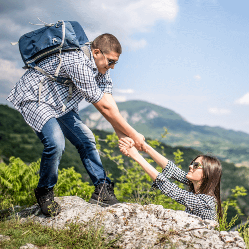 helping hand Man pulling woman from ledge while hiking.